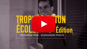 Un homme souriant, vêtu de lunettes, se tient debout devant une fenêtre. Texte : "Trophée Béton Écoles 7e Édition. Troisième Prix : Alexandre Puech." Un symbole lecture vidéo apparaît.