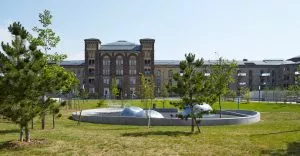 Bâtiment en brique, entouré de pelouse et de jeunes arbres, avec une installation circulaire en béton et dômes métalliques au premier plan, sous un ciel dégagé.