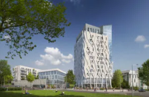 Un édifice moderne à la façade géométrique se dresse. Des passants marchent, certains à vélo, près d'un parc verdoyant avec des arbres, sous un ciel bleu parsemé de nuages.