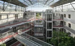 Un bâtiment avec des passerelles métalliques relie plusieurs étages. Les passerelles permettent la circulation entre les parties du bâtiment. Un toit en verre laisse passer la lumière naturelle, illuminant l'intérieur.