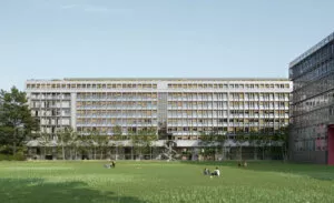 Un grand bâtiment moderne aux nombreuses fenêtres, entouré d'arbres, s’élève à l’arrière d’une vaste pelouse verte. Plusieurs personnes sont assises sur l'herbe par une journée ensoleillée.
